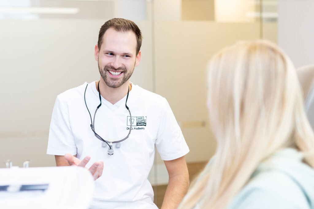 Junge blonde Frau erhält Zahnästhetik Beratung vom jungen Zahnarzt in einem hellen modernen Behandlungszimmer